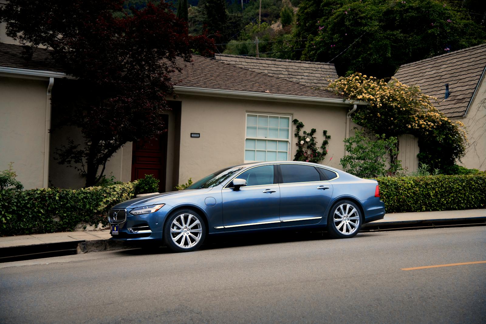 home and auto, sleek blue luxury car parked in front of a suburban house with greenery.